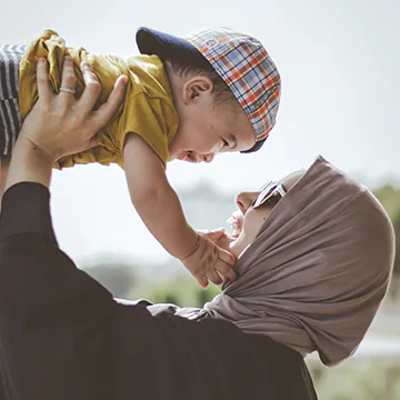 Muslim woman holding a smiling baby boy up in the air