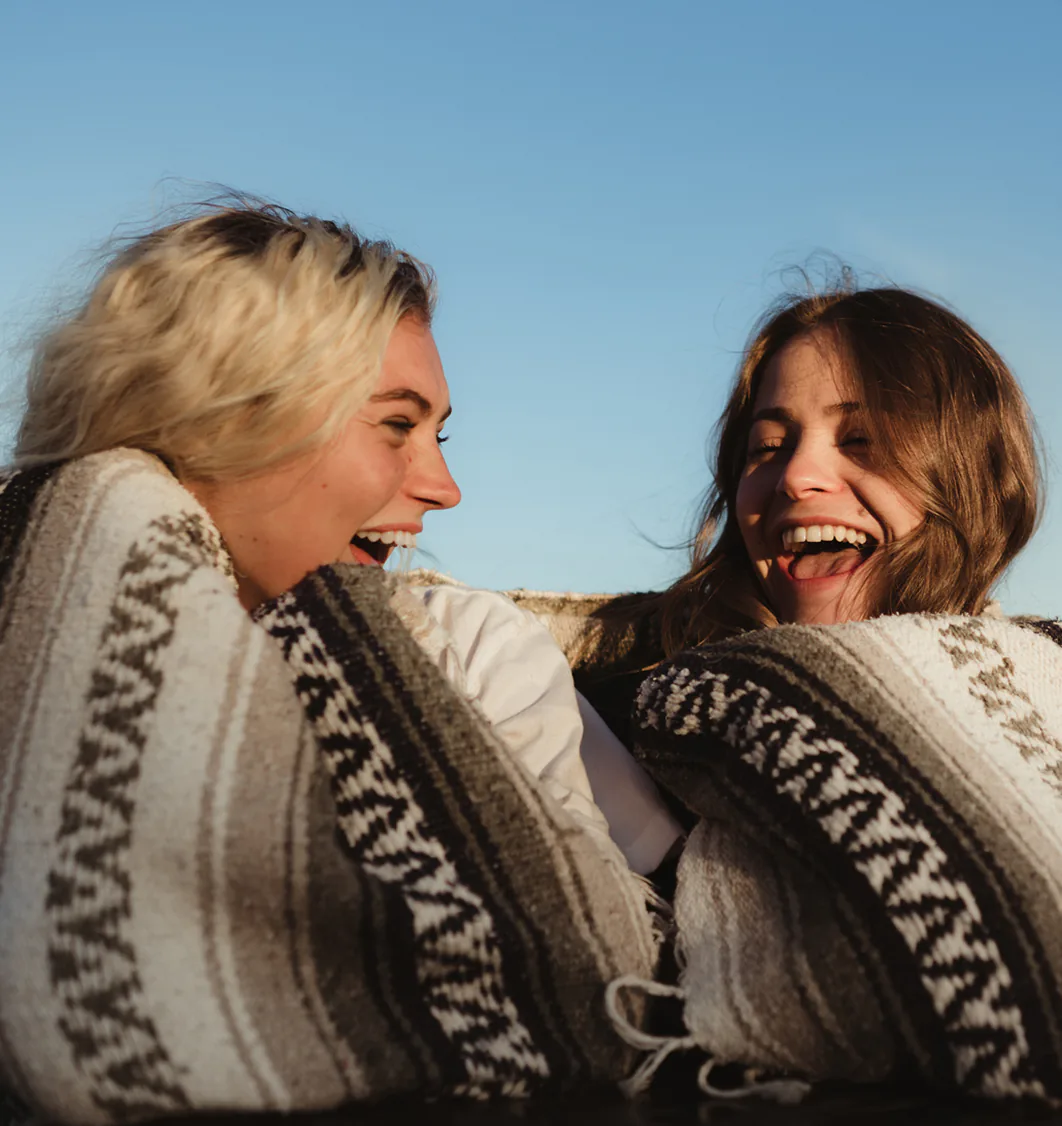 Two young women sharing a laugh while wrapped in a blanket